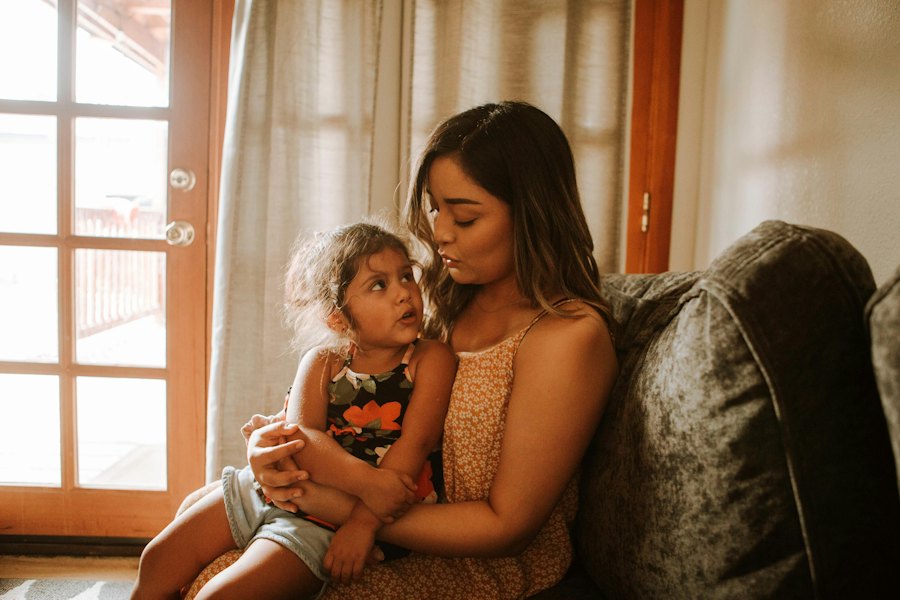 A mother on a sofa holds her toddler, who gazes up at her.