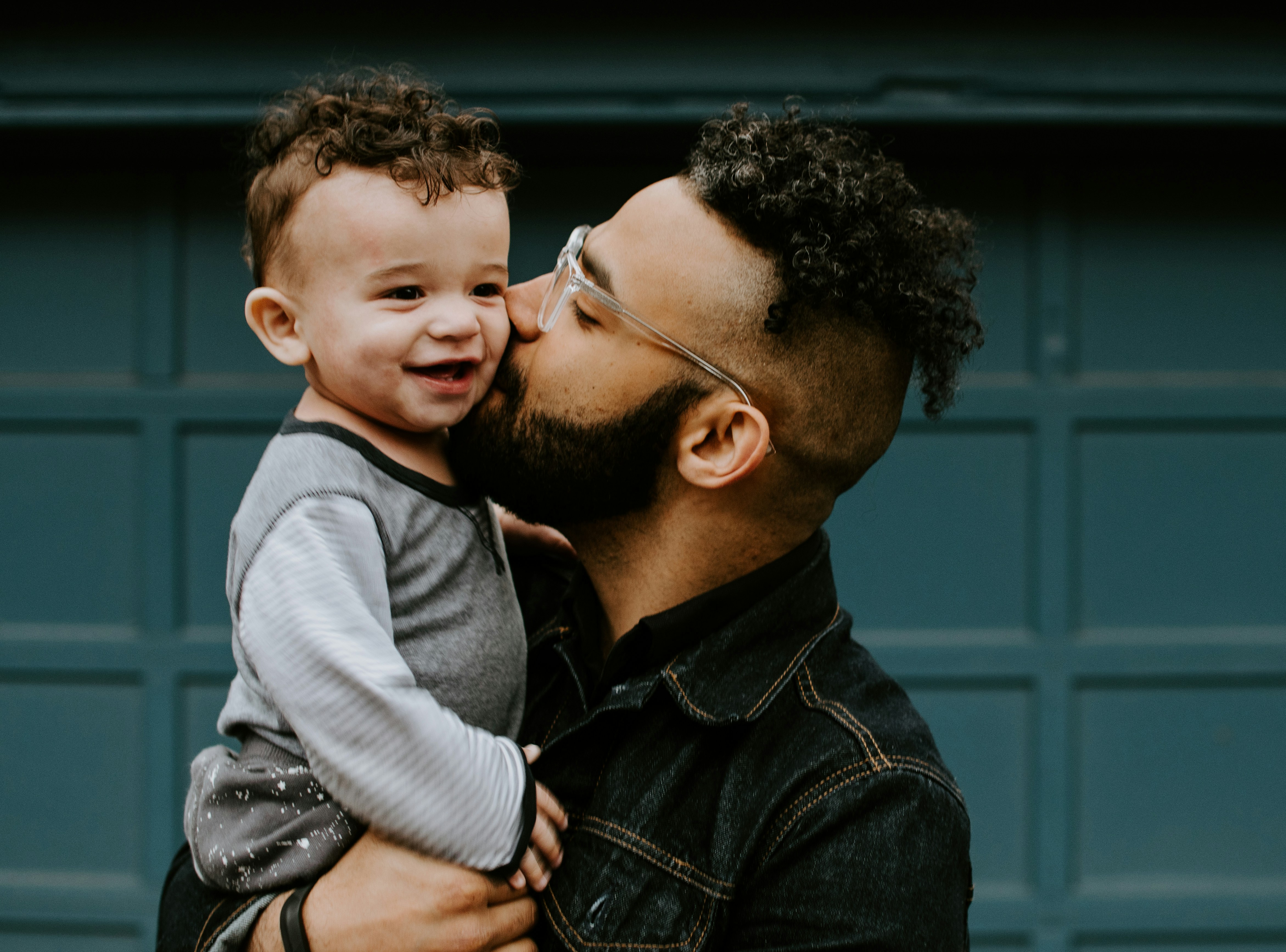 A father is holding his daughter, giving her a kiss.