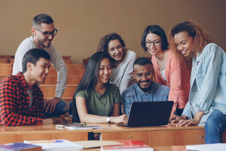 A diverse group of college students collaborate around a laptop in a lecture hall.