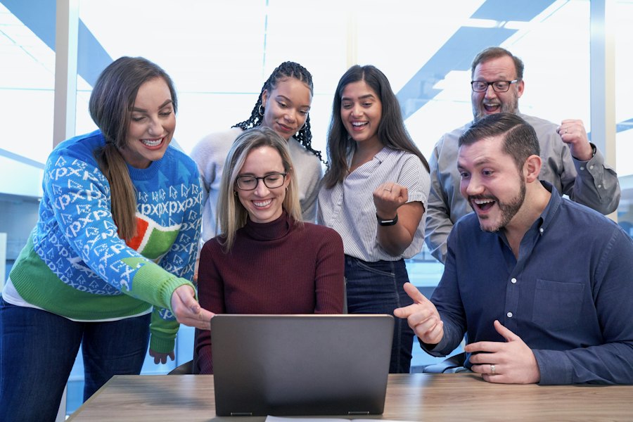 Students and an instructor gather around a laptop, discussing their work.